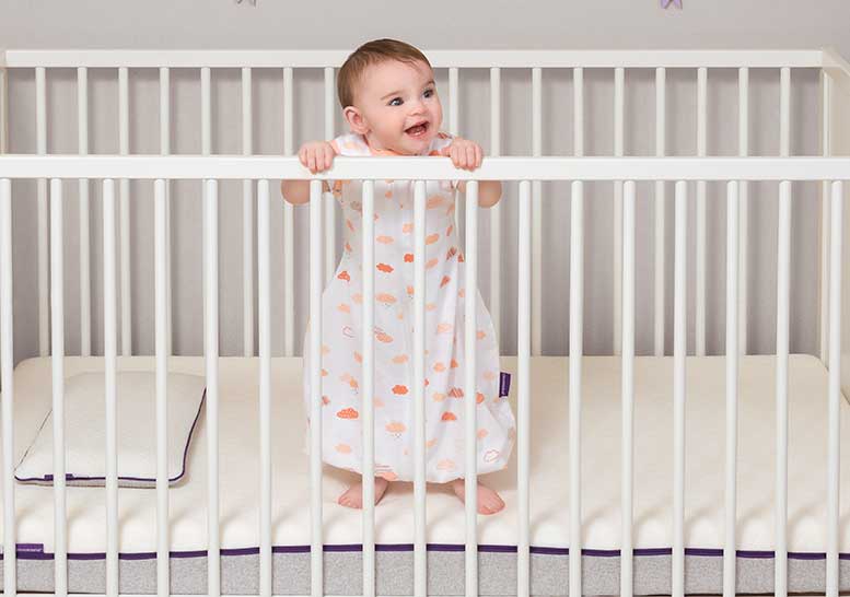 baby standing in cot wearing a sleep suit