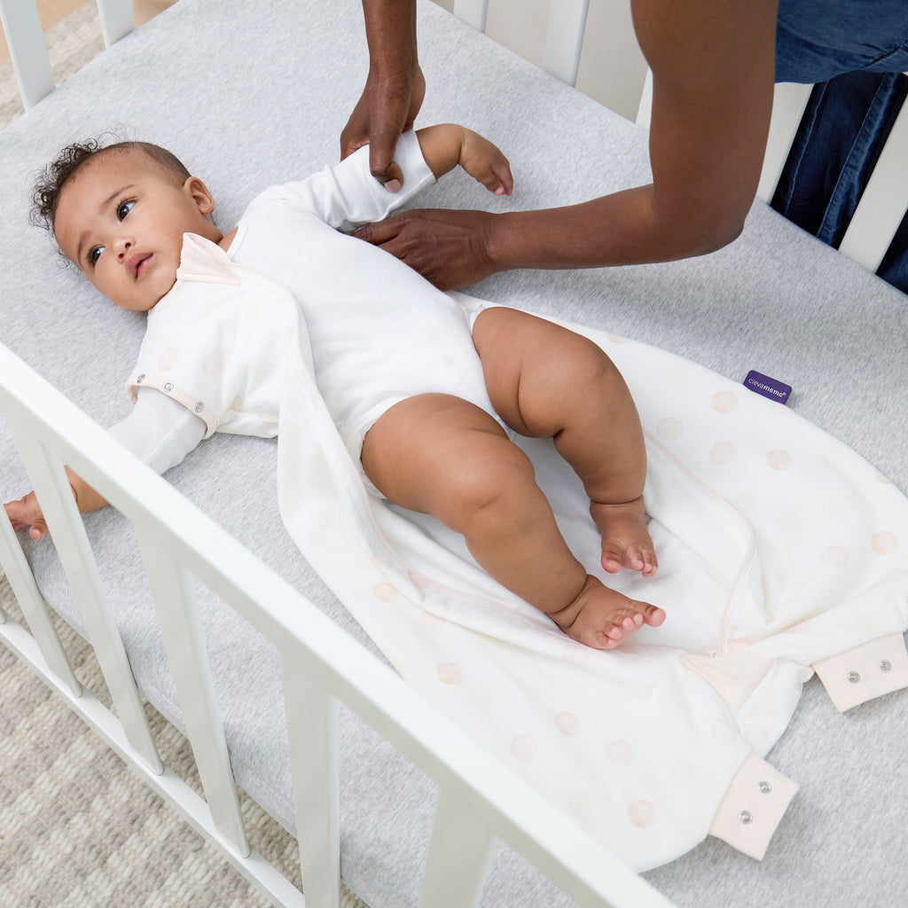 Baby lying in a crib with a person adjusting the baby's dreamsuit