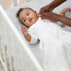 Baby lying in a crib with a person adjusting the baby's clevasleep dreamsuit