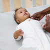 Baby lying in a crib  wearing a dreamsuit with a person's hand reaching out
