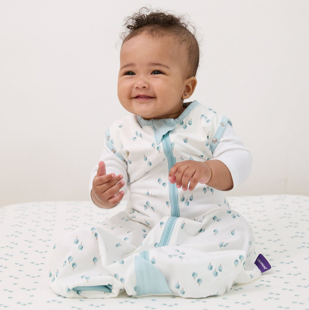 Baby wearing a watercolour foresr dreamsuit , sitting on a sheet in the same pattern.