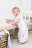 Child in a blue dot clevasleep dreamsuit standing next to a beige stool in a nursery.